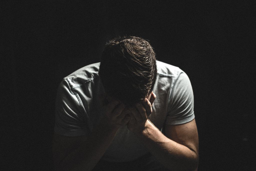 A man is experiencing a panic attack and has his head in his hands. He is thinking about reaching out to an online anxiety counselor | Online Therapy for Anxiety | Synergy eTherapy