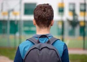 College student walking with a backpack. He experiences anxiety related to school and the pressure to perform well. He is on his way to attend an online therapy session.