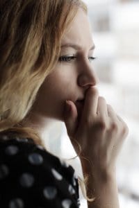 Sad woman looking out the window with her hand over her mouth before attending online therapy for trauma with synergy eTherapy in the state of Kansas.