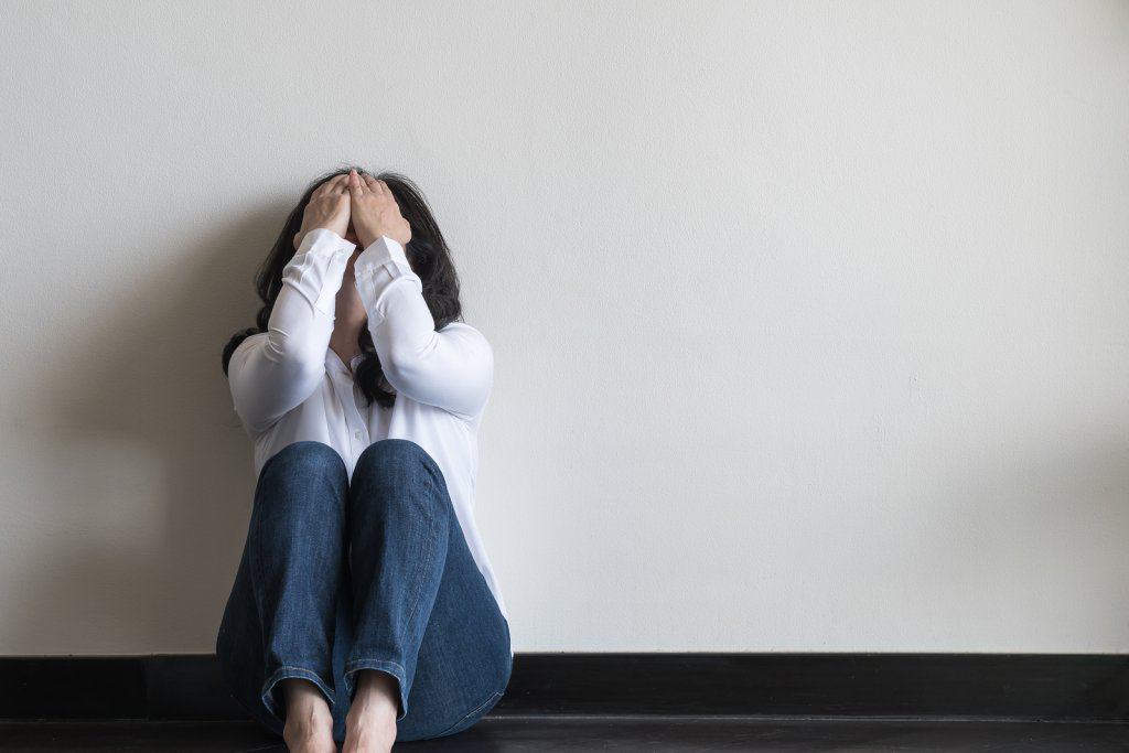 woman suffering from depression sits against a wall holding her head in her hands. She goes to online depression treatment with Synergy eTherapy an online counseling practice