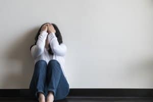 woman suffering from depression sits against a wall holding her head in her hands. She goes to online depression treatment with Synergy eTherapy, an online counseling practice