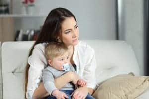 woman copes with postpartum depression while holding her infant son. She gets maternal mental health therapy from a Synergy eTherapy online therapist