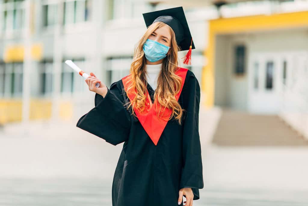 Happy graduate wearing a mask. She meets with an online therapist to get help dealing with grief. Learn more from Synergy ETherapy
