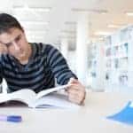 stressed out college student studying in the library. He goes to online therapy for college students with Synergy eTherapy. Start online counseling or online therapy for telehealth now!